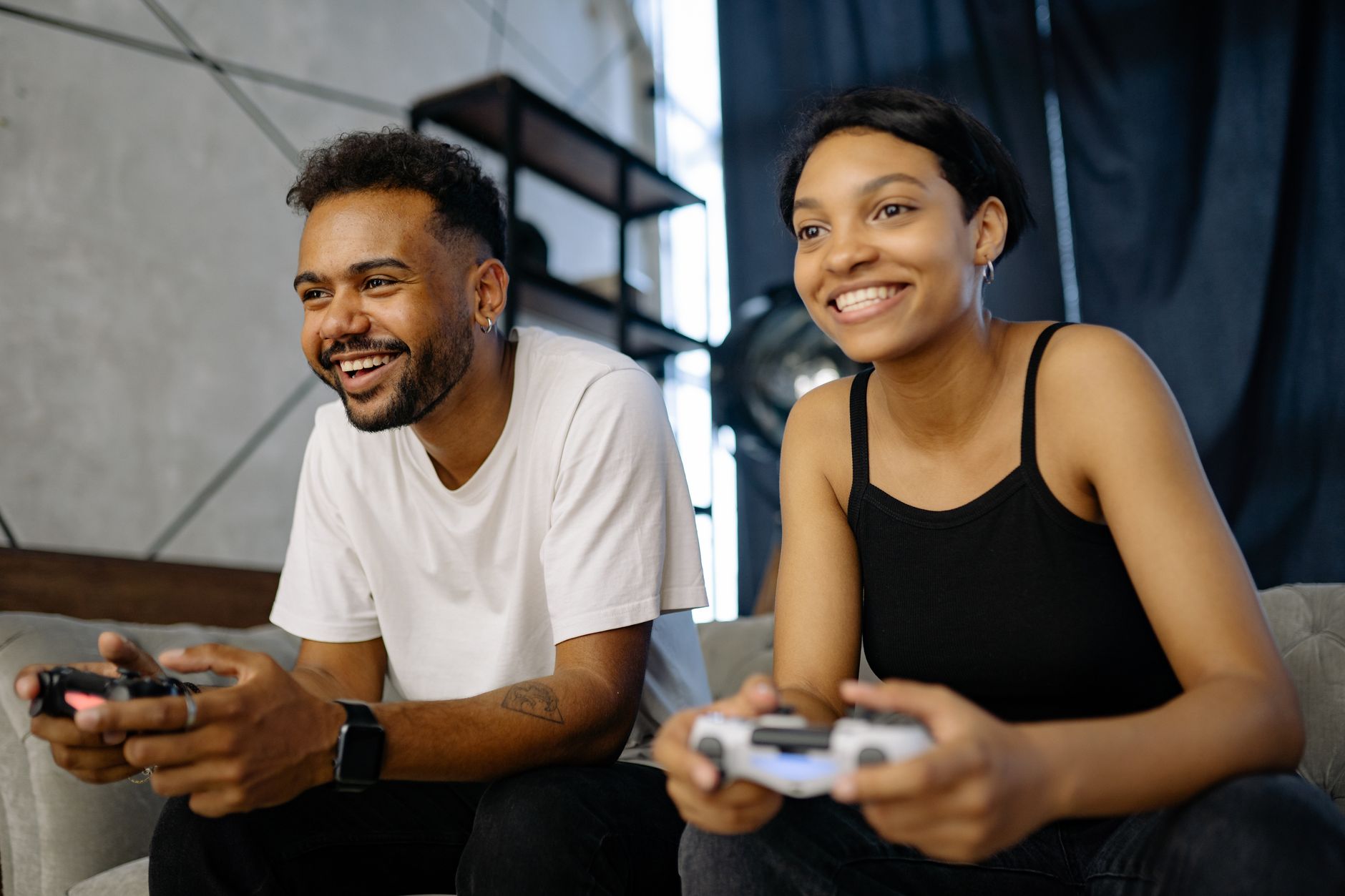 A couple playing video games on a sofa, engaged and smiling indoors.