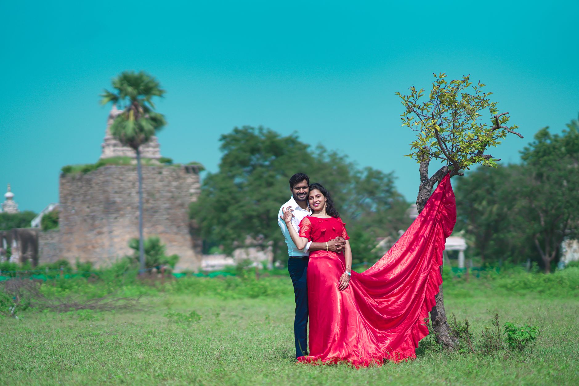 Couple embracing in a vibrant red dress with Golconda Fort in the background.