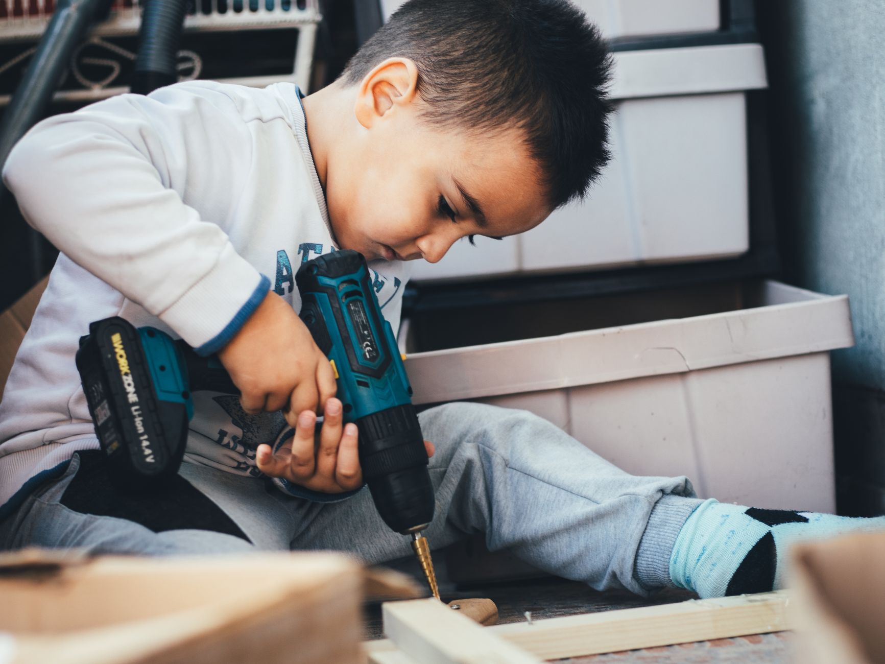 Young boy using a power drill to complete a DIY project at home.