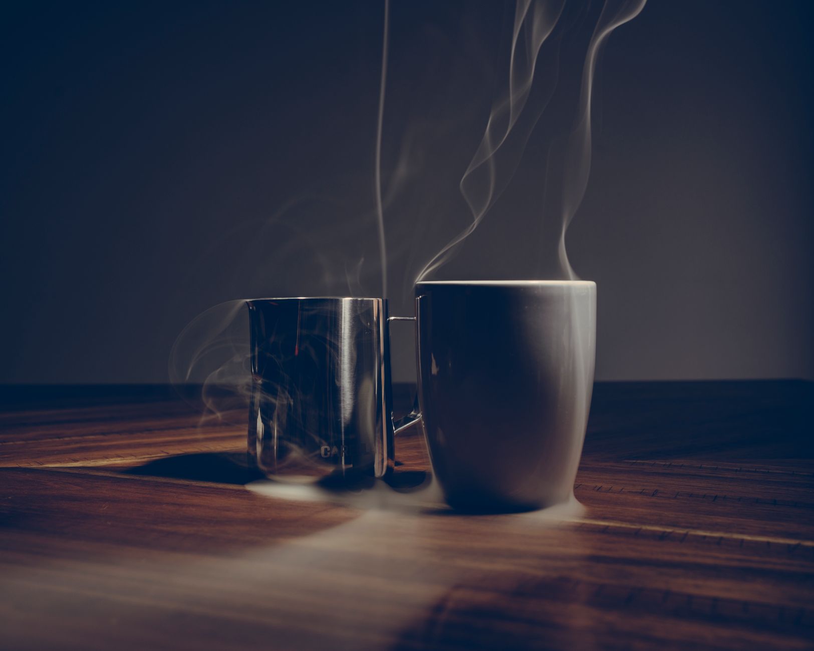 Two steaming coffee mugs on a wooden table create a cozy, warm ambiance.