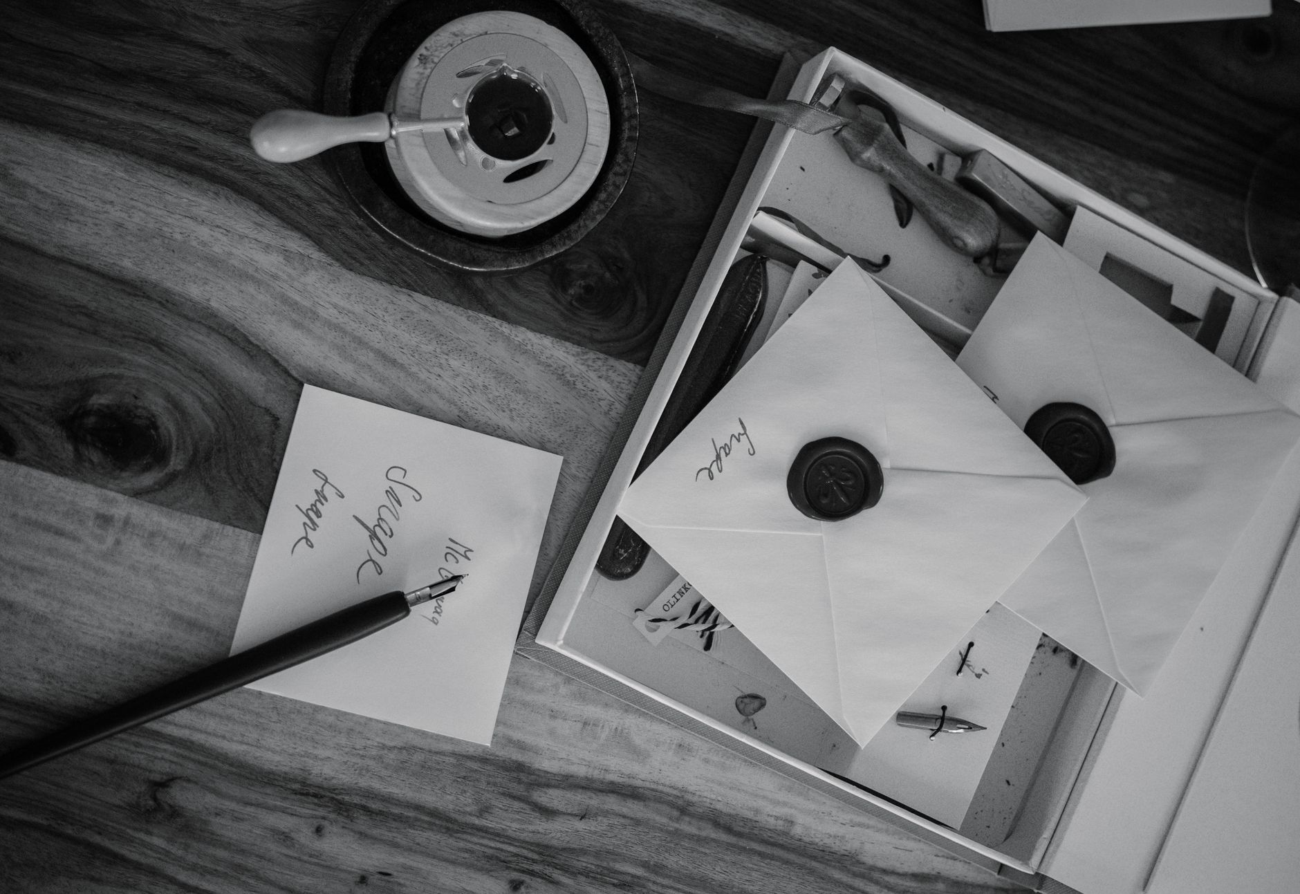 Black and white photo of vintage envelopes with wax seals and calligraphy tools on a wooden desk.
