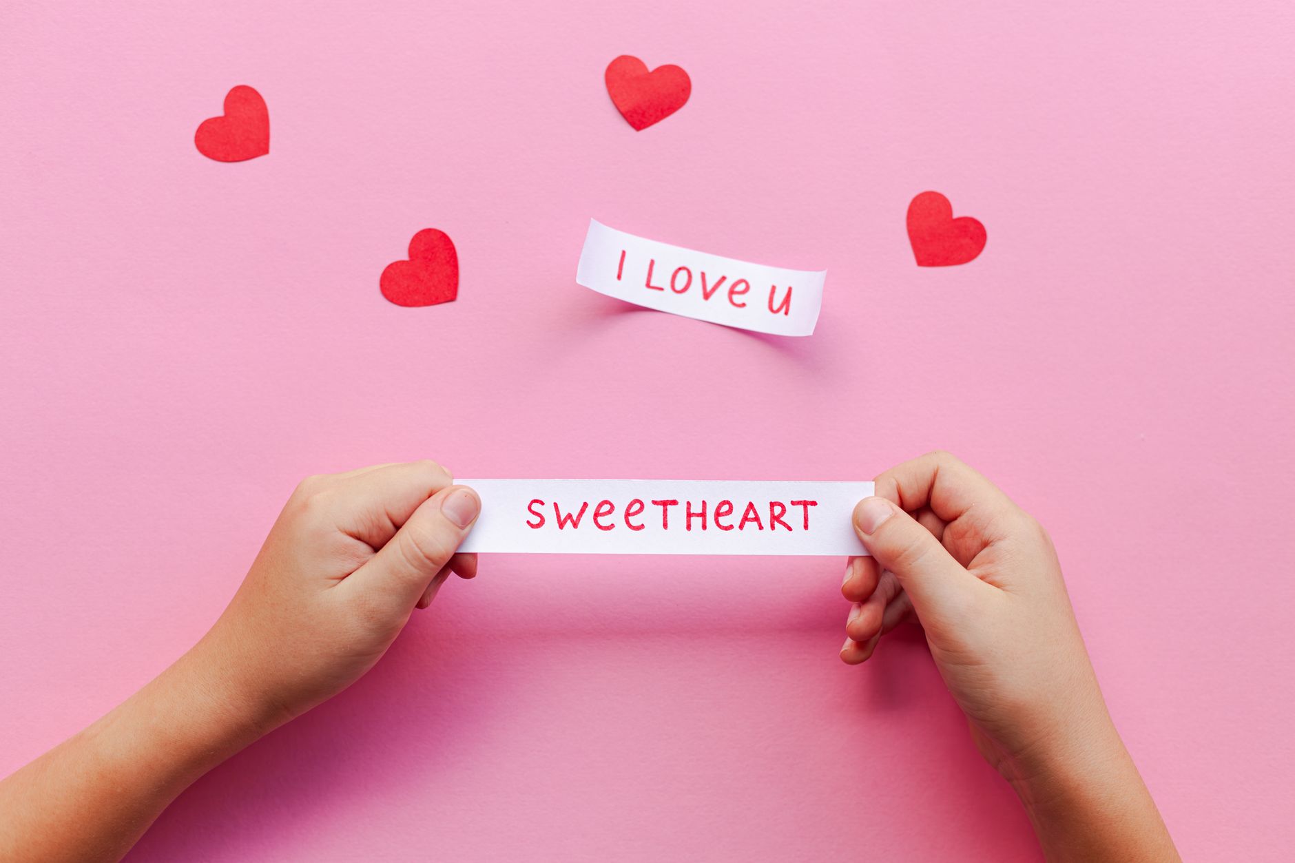 Hands holding love notes on pink background with red hearts. Perfect for Valentine's Day.