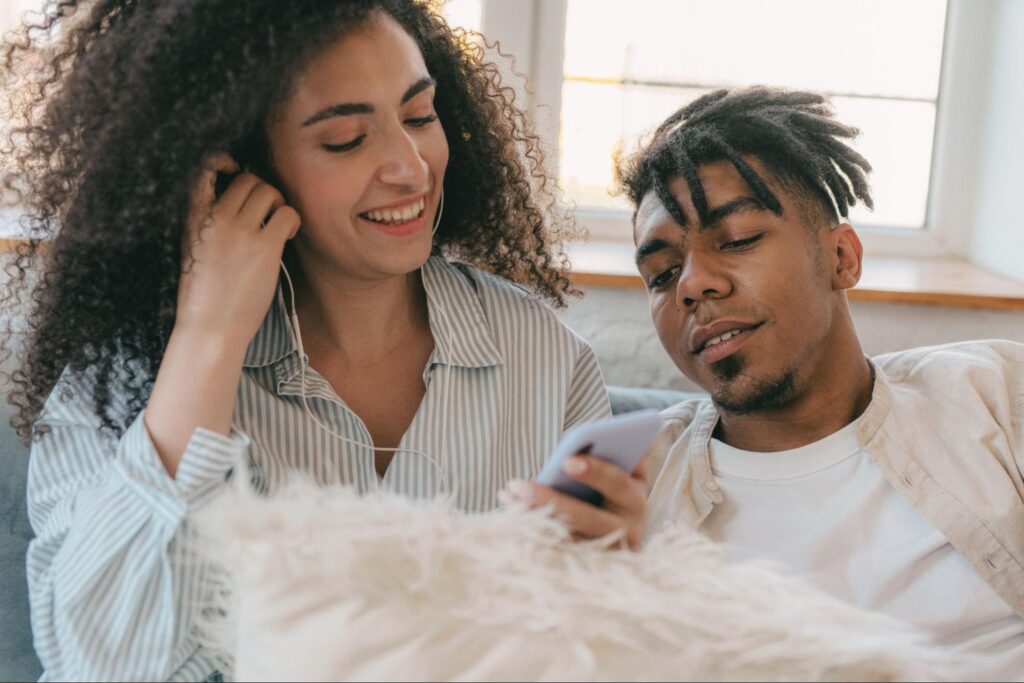 Couple sitting close together sharing earbuds and looking at a phone