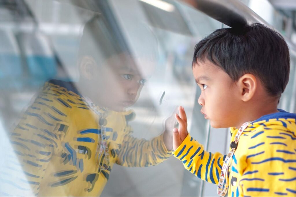 Young boy studying his own reflection in a window
