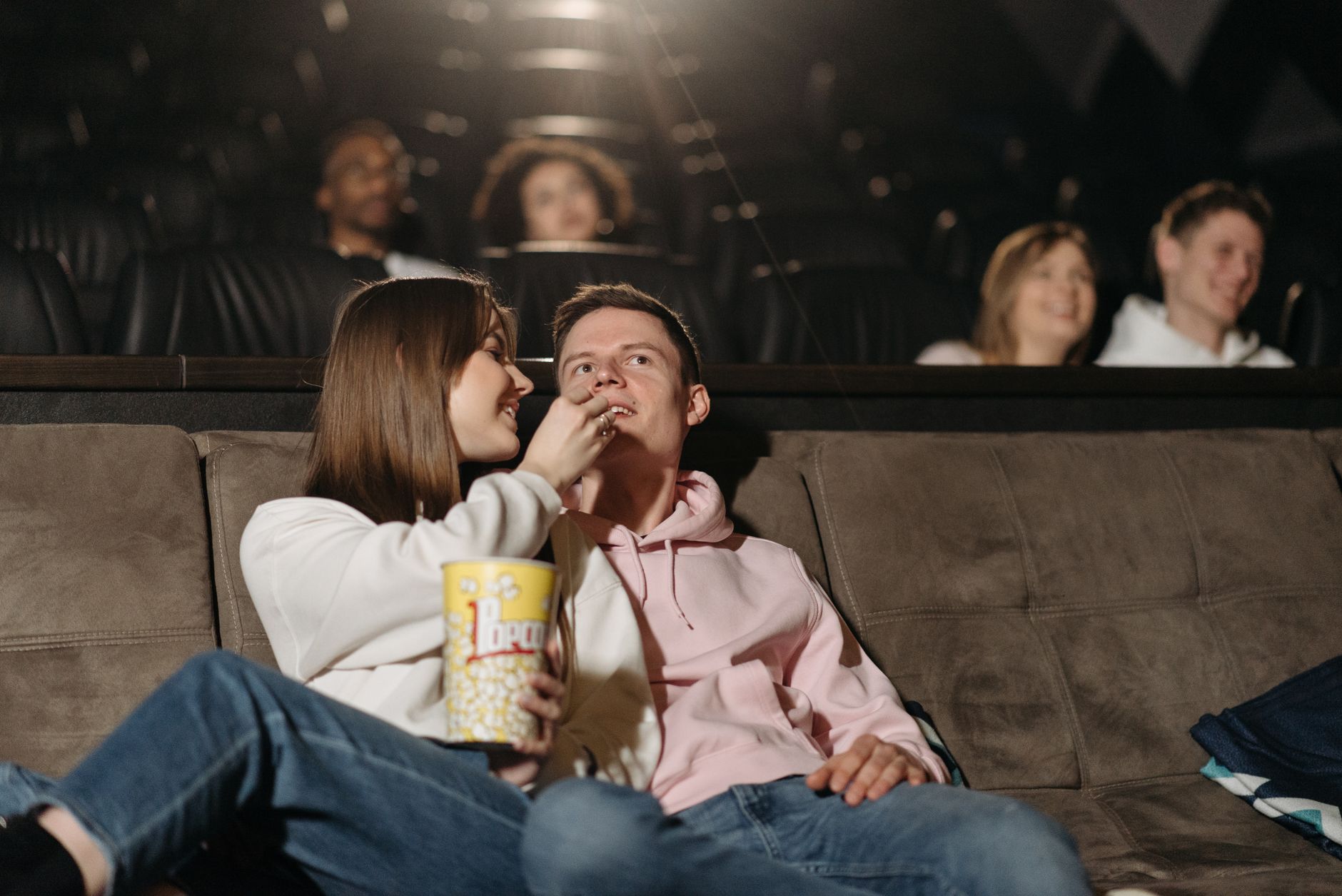 Couple enjoying a cozy movie night at the cinema, sharing popcorn in a relaxed setting.