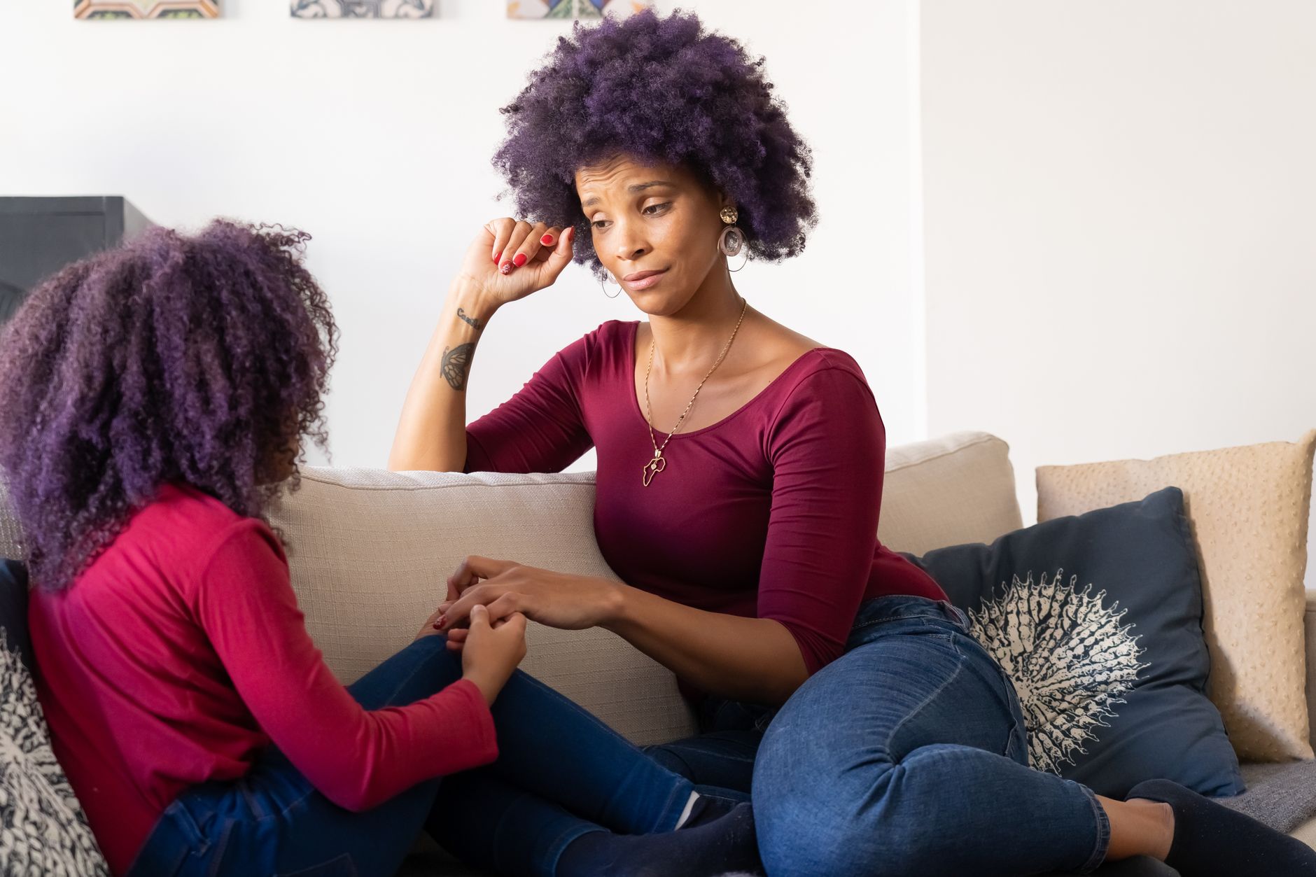 Mother and daughter with purple hair holding hands on the couch, sharing a moment of bonding and connection.