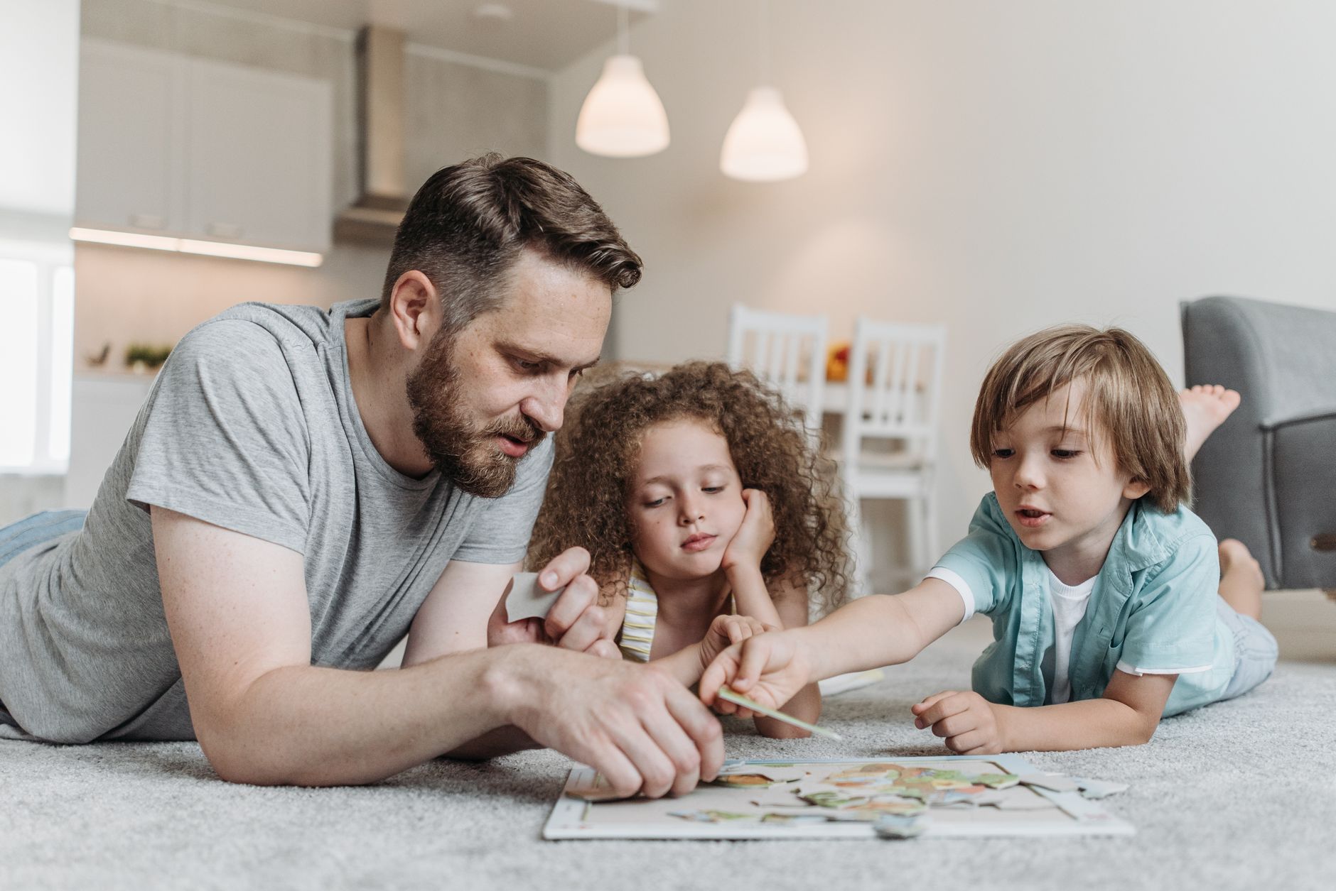 A father and two children engaged in solving a puzzle on the living room floor, fostering family bonding.