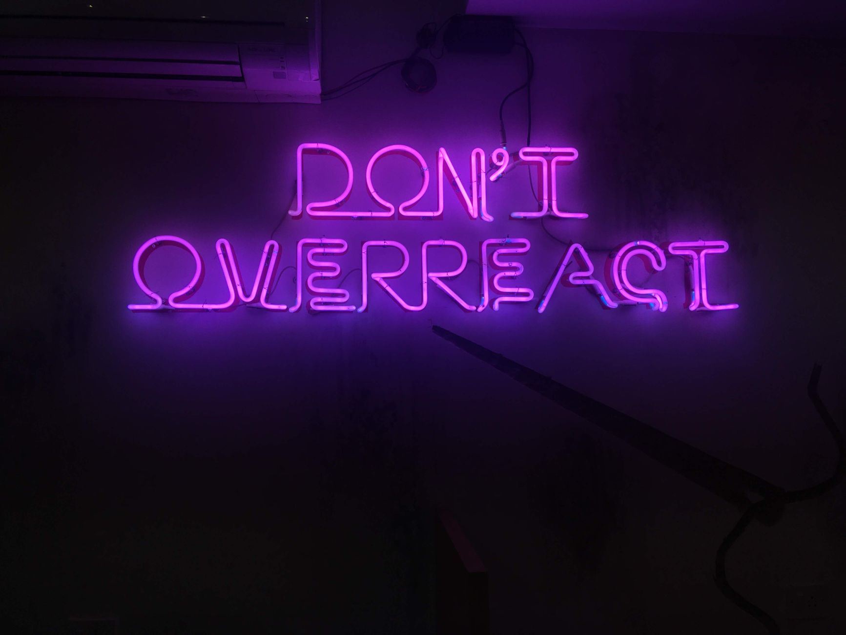 Purple neon sign with the message 'Don't Overreact' against a dark background.
