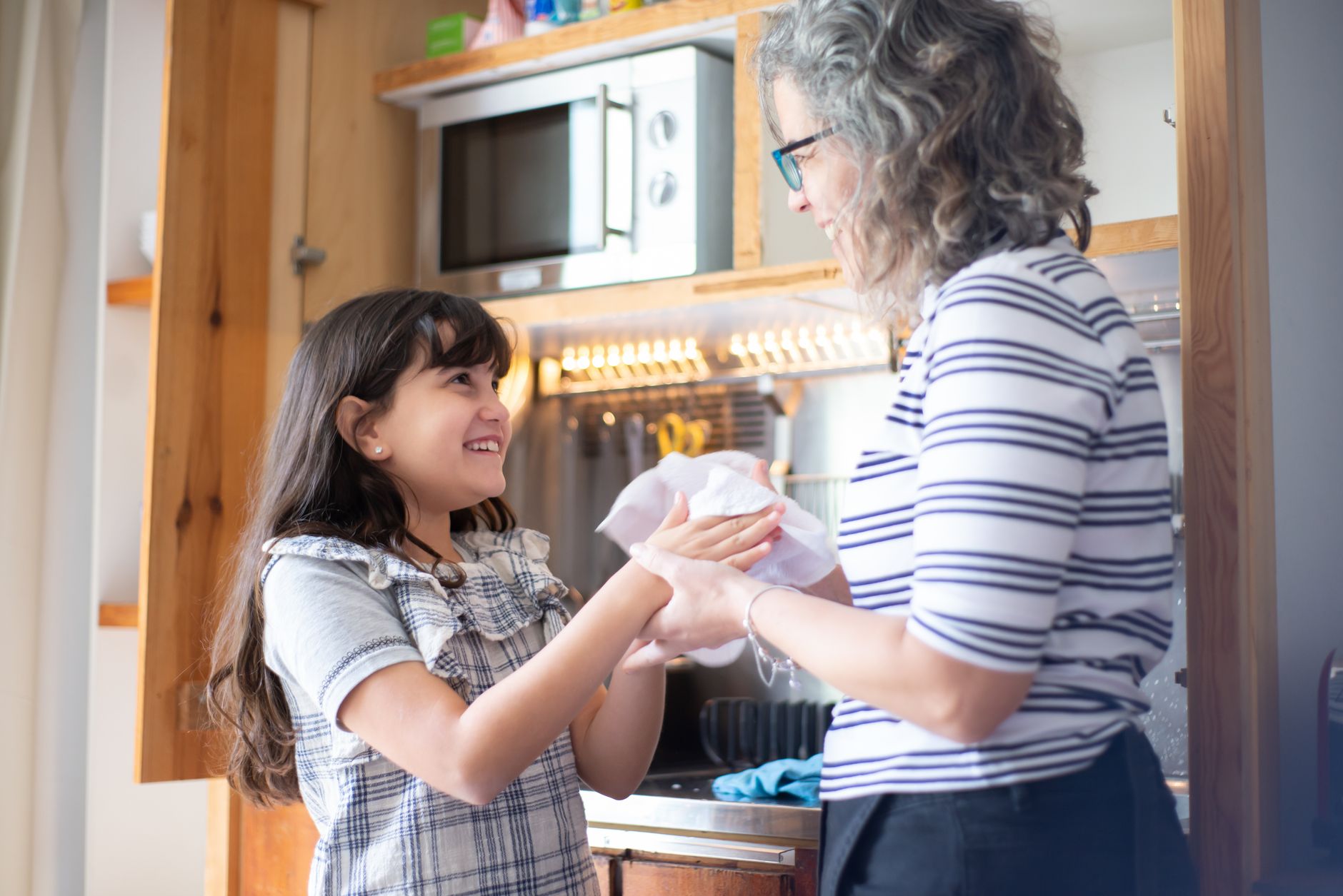 Mother bonding with daughter while drying hands in a cozy kitchen setting.