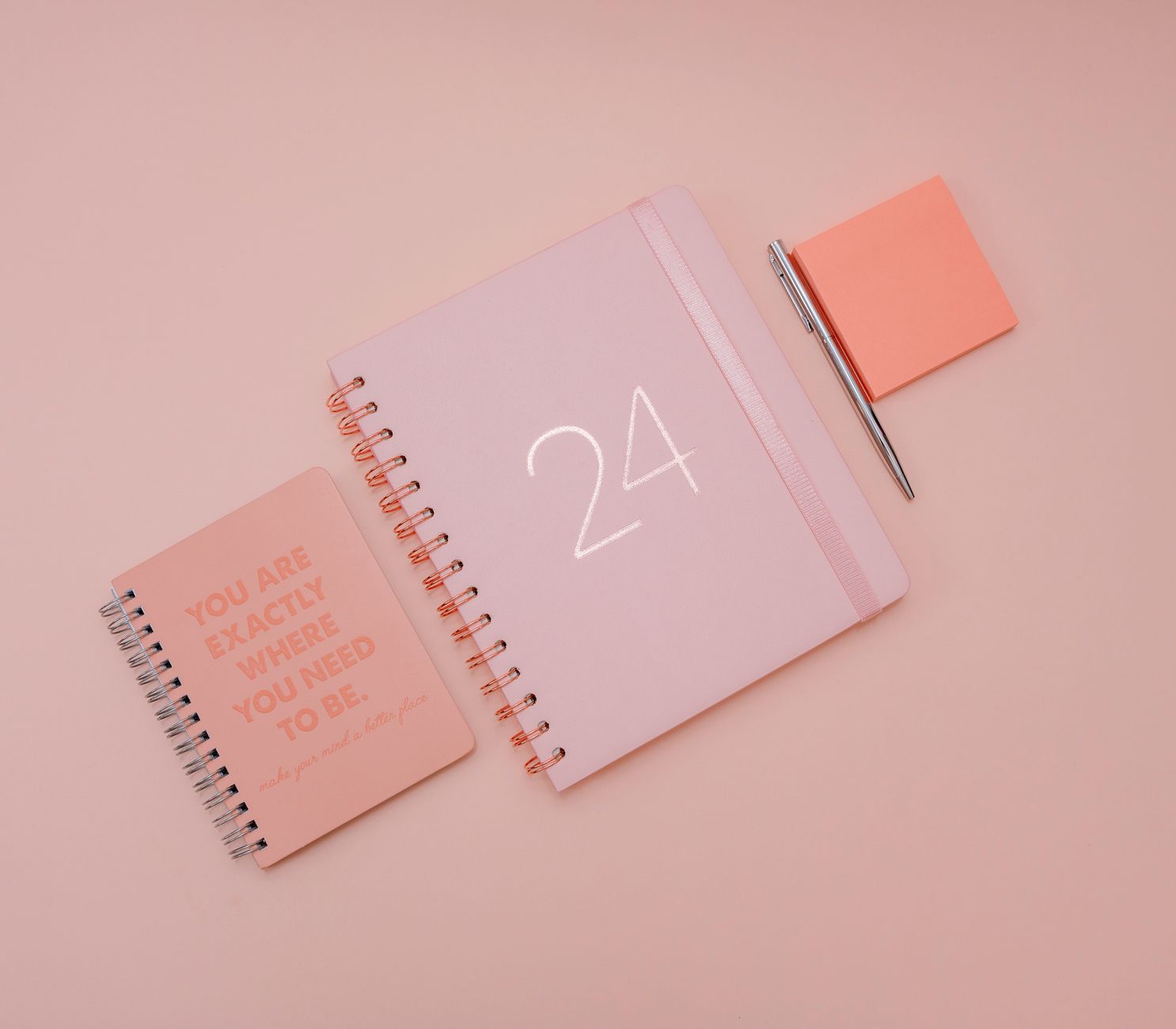 Aesthetic flat lay of a pink planner and notebook on a pastel background with motivational text.