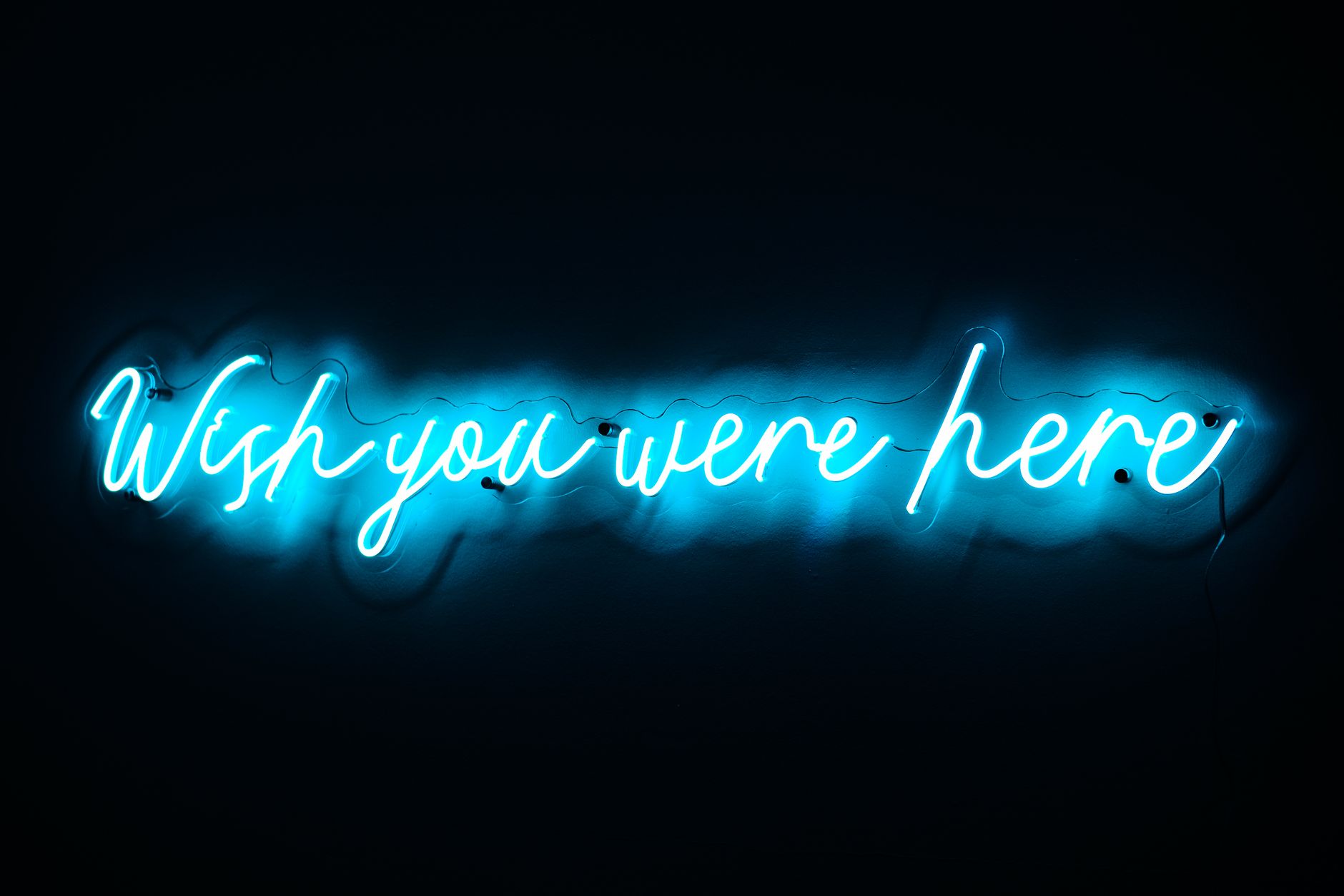 Blue neon sign displaying 'Wish you were here' on a dark background.