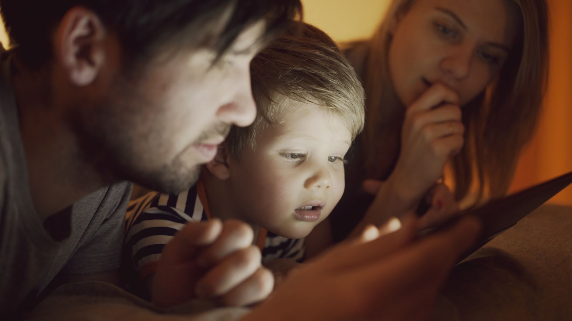 A family of three, including parents and a child, intently watching a digital tablet together indoors.